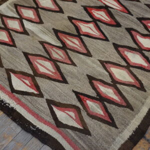 Flatweave rug featuring brown, red, and cream diamonds on a gray field over distressed wooden floorboards.