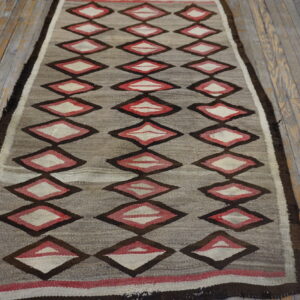 Flatweave rug runner in gray, red, and dark brown diamond patterns on worn wooden floors.