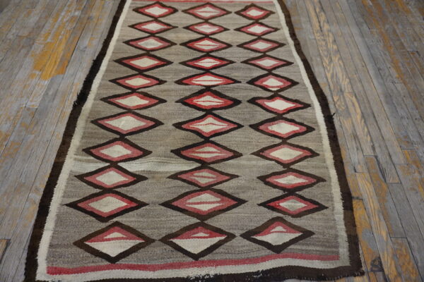 Flatweave rug runner in gray, red, and dark brown diamond patterns on worn wooden floors.
