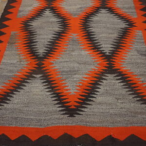 Bold orange and black geometric rug with a grey field lying on light, distressed wood flooring.