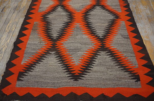Bold orange and black geometric rug with a grey field lying on light, distressed wood flooring.