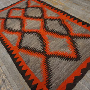 A gray, orange, and brown flatweave rug with serrated diamond patterns rests on distressed gray hardwood flooring.