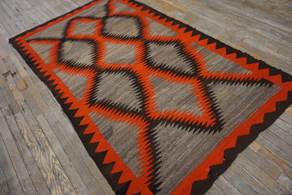 A gray, orange, and brown flatweave rug with serrated diamond patterns rests on distressed gray hardwood flooring.