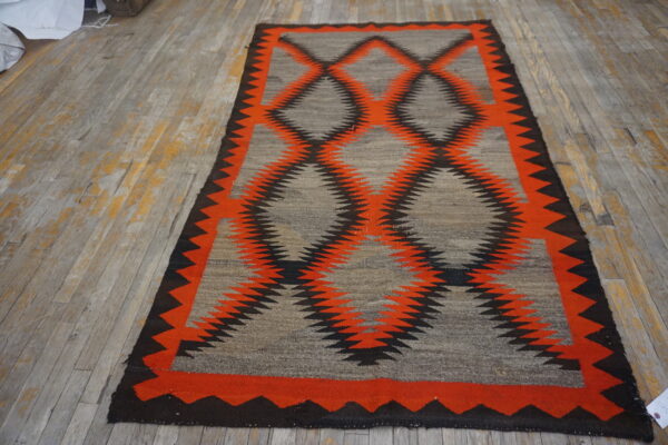Gray flatweave rug featuring a bold orange and black geometric zigzag diamond pattern on wood flooring.