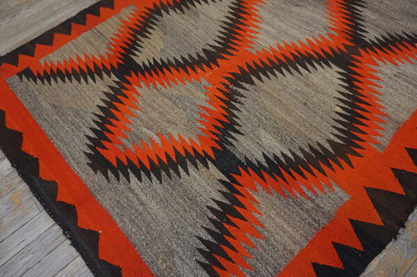 Gray, orange, and black geometric flatweave rug with serrated diamonds resting on light wooden plank flooring.