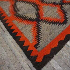Flat-woven rug in orange, black, and gray with a zigzag geometric design on rustic wood floors.