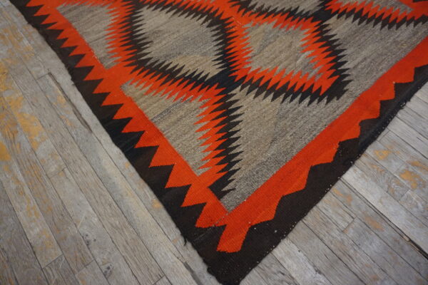 Flat-woven rug in orange, black, and gray with a zigzag geometric design on rustic wood floors.