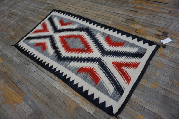 Flatweave rug featuring bold serrated diamonds in red, black, gray, and cream on distressed wood flooring.
