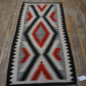 Black, red, gray, and white geometric runner rug resting on a distressed wood plank floor.