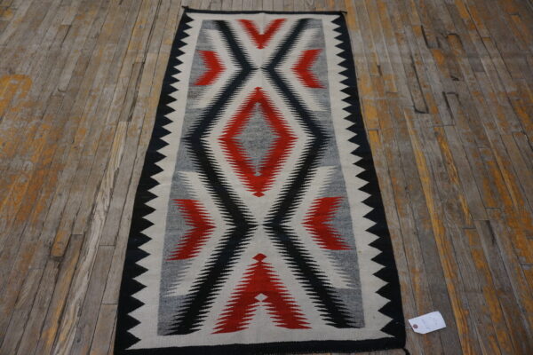 Black, red, gray, and white geometric runner rug resting on a distressed wood plank floor.