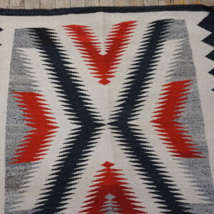 Flatwoven rug featuring a serrated geometric pattern in red, black, gray, and white on wood flooring.
