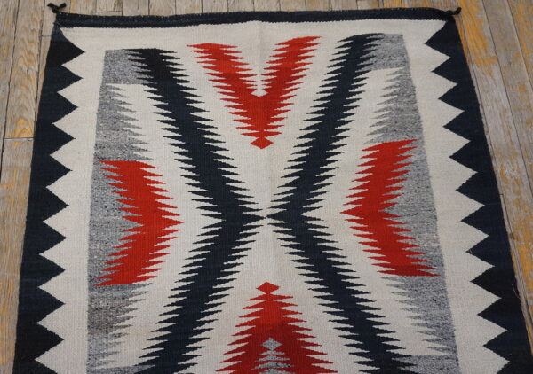 Flatwoven rug featuring a serrated geometric pattern in red, black, gray, and white on wood flooring.
