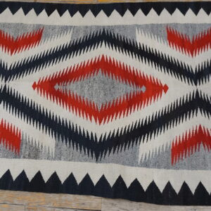 Geometric flatweave rug with jagged red, black, and gray diamonds displayed on rustic wood flooring.