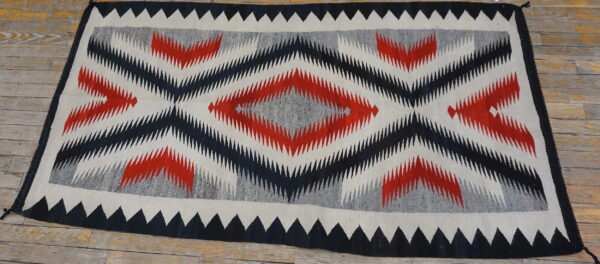 Geometric flatweave rug with jagged red, black, and gray diamonds displayed on rustic wood flooring.