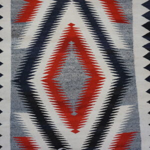 Low-pile rug with interlocking red, black, grey, and white serrated diamond pattern on wood planks.