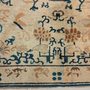Textured rug detail with stylized floral and geometric patterns in beige, teal blue, and brown colors.