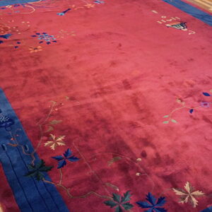 Deep red high-pile rug featuring a wide navy blue border and scattered colorful floral designs on wood flooring.