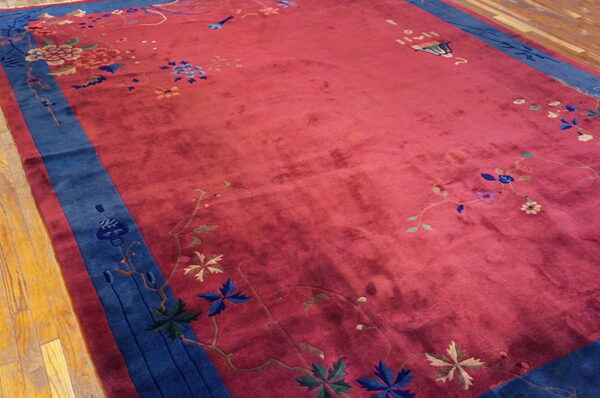 Deep red high-pile rug featuring a wide navy blue border and scattered colorful floral designs on wood flooring.