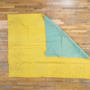 Yellow and aqua reversible quilted textile with stitched patterns displayed on natural wood flooring.