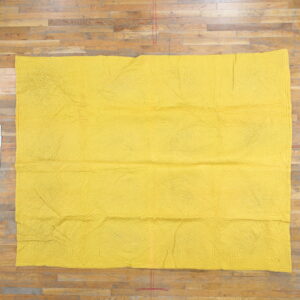 Solid yellow textile featuring an overall low-relief stitched pattern displayed on plank wood flooring.