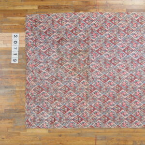 A low-pile rug featuring a dusty pink, red, and blue floral and geometric diamond pattern on wood planks.