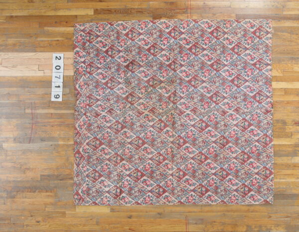 A low-pile rug featuring a dusty pink, red, and blue floral and geometric diamond pattern on wood planks.