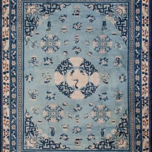 Light blue rug featuring dark blue and beige traditional patterns, including wide borders, on a hardwood floor.