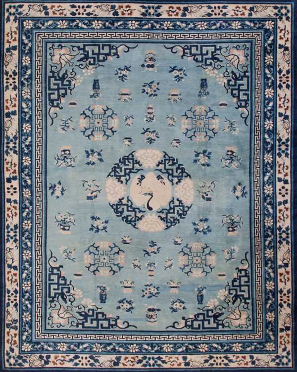 Light blue rug featuring dark blue and beige traditional patterns, including wide borders, on a hardwood floor.