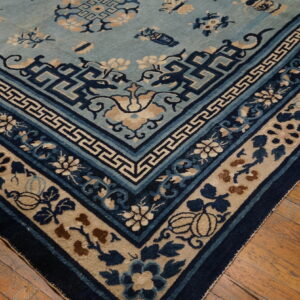 Detailed light blue rug corner featuring dark blue geometric and floral borders on wood flooring.