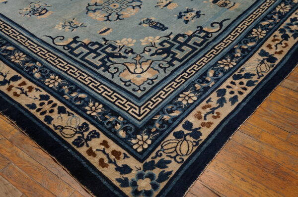 Detailed light blue rug corner featuring dark blue geometric and floral borders on wood flooring.
