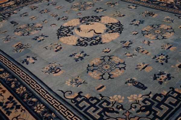 Light blue rug featuring navy geometric borders, scattered tan floral motifs, and a central crane design.