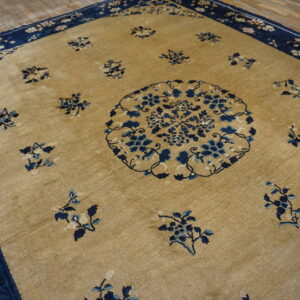 Tan rug with a central blue floral medallion and scattered blue motifs on wooden flooring.