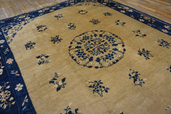 Tan rug with a central blue floral medallion and scattered blue motifs on wooden flooring.