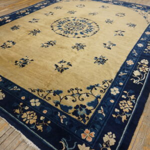 Gold-field rug with dark blue floral borders and scattered motifs rests upon worn wooden flooring.