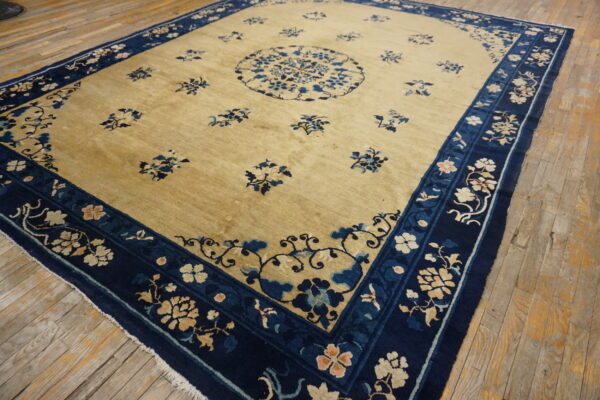 Gold-field rug with dark blue floral borders and scattered motifs rests upon worn wooden flooring.