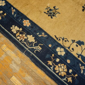 A gold and navy floral-patterned rug lies diagonally on rustic yellow hardwood flooring.