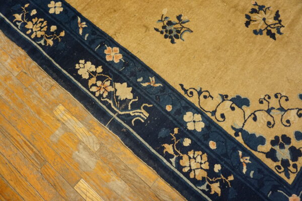 A gold and navy floral-patterned rug lies diagonally on rustic yellow hardwood flooring.