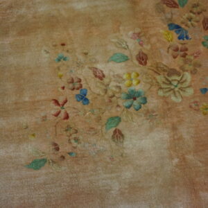 Distressed tan rug features scattered floral motifs in muted blue, yellow, green, and rust.