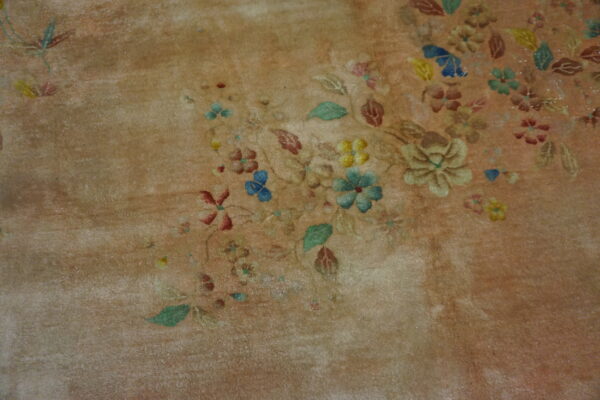 Distressed tan rug features scattered floral motifs in muted blue, yellow, green, and rust.