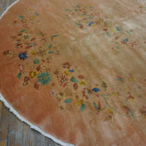 Circular dusty peach rug featuring a delicate multicolored floral vine pattern on distressed wooden floorboards.