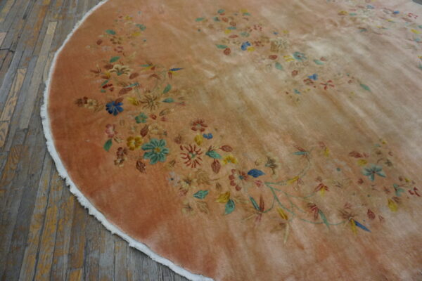 Circular dusty peach rug featuring a delicate multicolored floral vine pattern on distressed wooden floorboards.