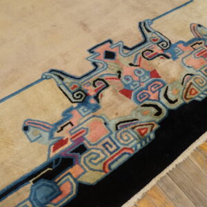 Beige rug with a vibrant, geometric blue, pink, and black border lying on wooden plank flooring.