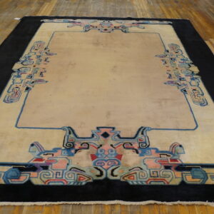 Cream rug with a wide black border and stylized blue and pink geometric patterns on hardwood flooring.