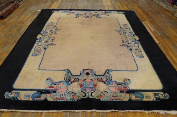 Cream rug with a wide black border and stylized blue and pink geometric patterns on hardwood flooring.