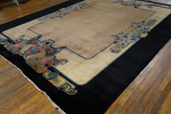 Tan rug with a black outer border and stylized colorful designs placed on plank wood flooring.