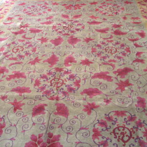 Grayish-taupe rug with sprawling magenta floral and vine motifs, bordered by a gold band on wooden flooring.