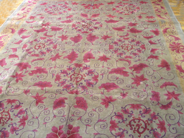Grayish-taupe rug with sprawling magenta floral and vine motifs, bordered by a gold band on wooden flooring.
