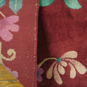 Deep maroon rug with pink and teal flowers is folded, showing the woven reverse side on wood.