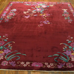 Large, deep red rug with colorful floral and vine motifs displayed on plank hardwood flooring.