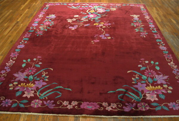 Large, deep red rug with colorful floral and vine motifs displayed on plank hardwood flooring.
